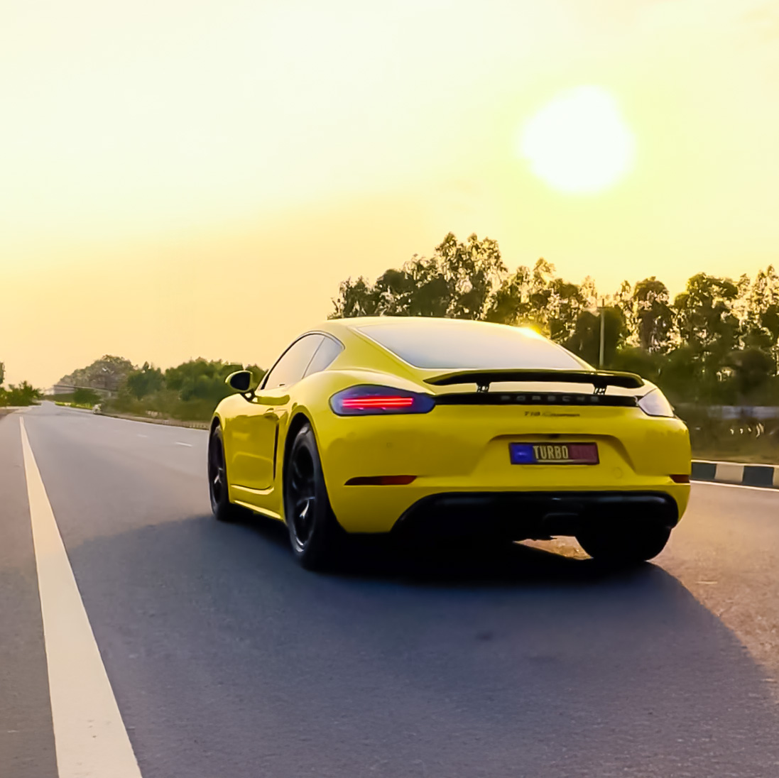 Yellow Porsche 718 Cayman driving on a sunny 15 KM highway ring road stretch